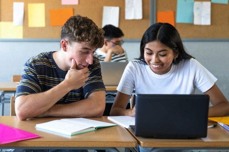 Caucasian teen boy and native american teenage female high school students in class using laptop.